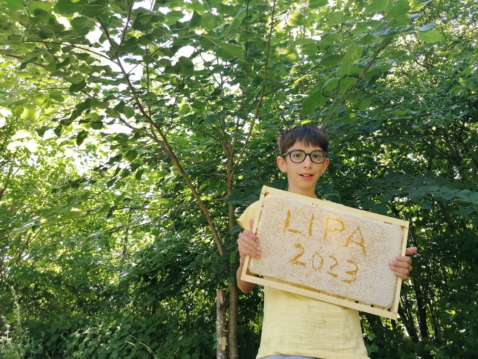 Mladi čebelar drži pokrit medeni sat z napisom Lipa 2023